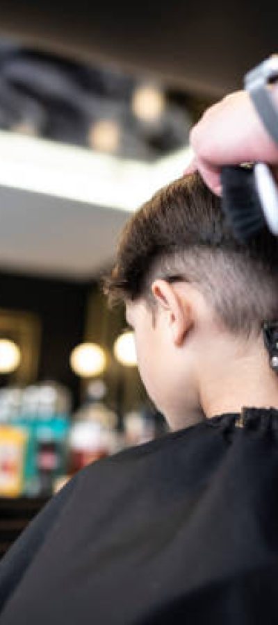 Little 7-year-old boy goes to a barbershop to get a modern haircut, indoors store working hairdresser real image